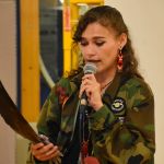 Photo of Cambria Harris speaking into a microphone and holding an eagle feather.