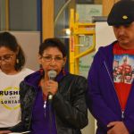 Sue Caribou speaks into a microphone with an Indigenous relative standing on either side of her.
