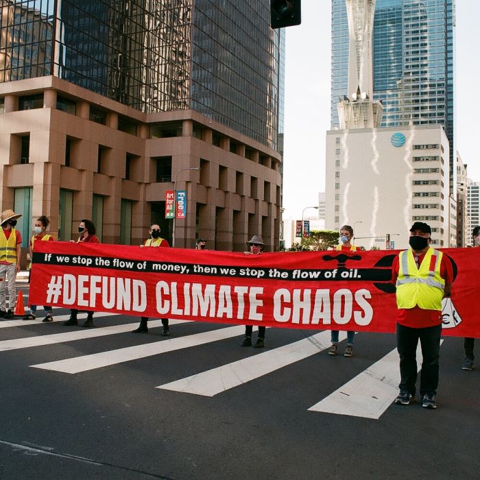 A group of people blocks a major downtown “Los Angeles” intersection crosswalk while holding a long horizontal banner that reads, to protest climate disaster financiers. Photo credit: Steph Viera, November 25, 2022