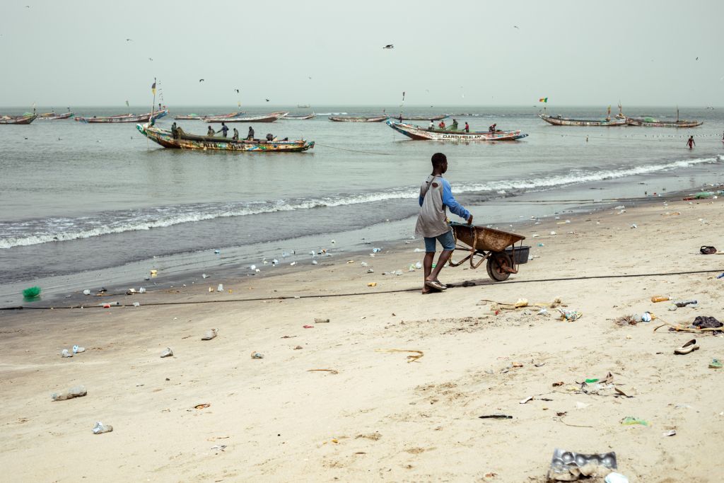 A young boy pushes a rusty wheelbarrow down the beach, in the Kartong, to help collect the catch of the day off of the fishing boats. Photo credit: Abubacar Fofana, February 24, 2024