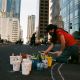 A woman paints the street along several people, with the buildings of BlackRock and Wells Fargo surrounding them. Photo credit: Steph Viera, November 25, 2022
