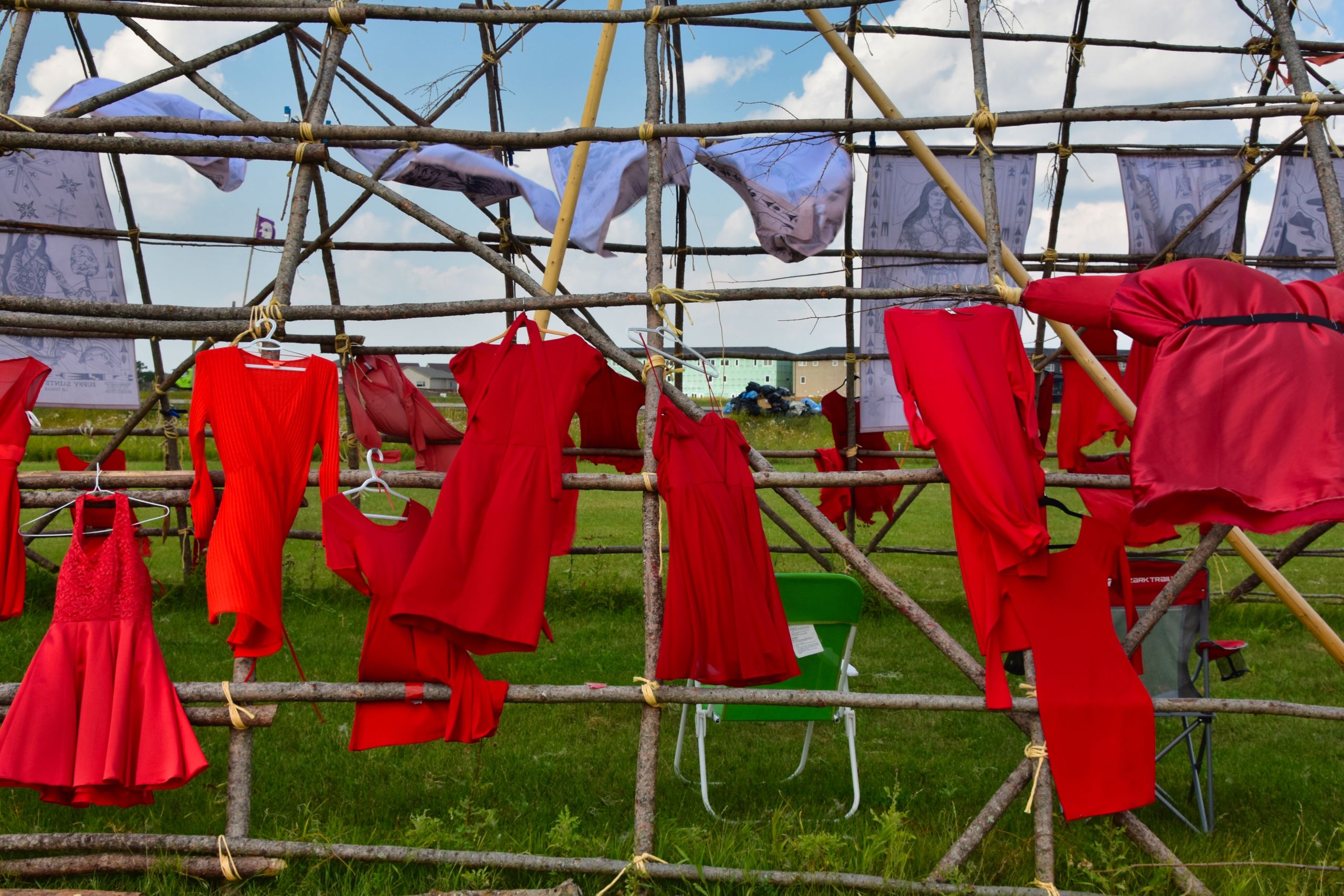 Numerous red dresses hang from the frame of a long house and blow in the breeze on sunny summer day.