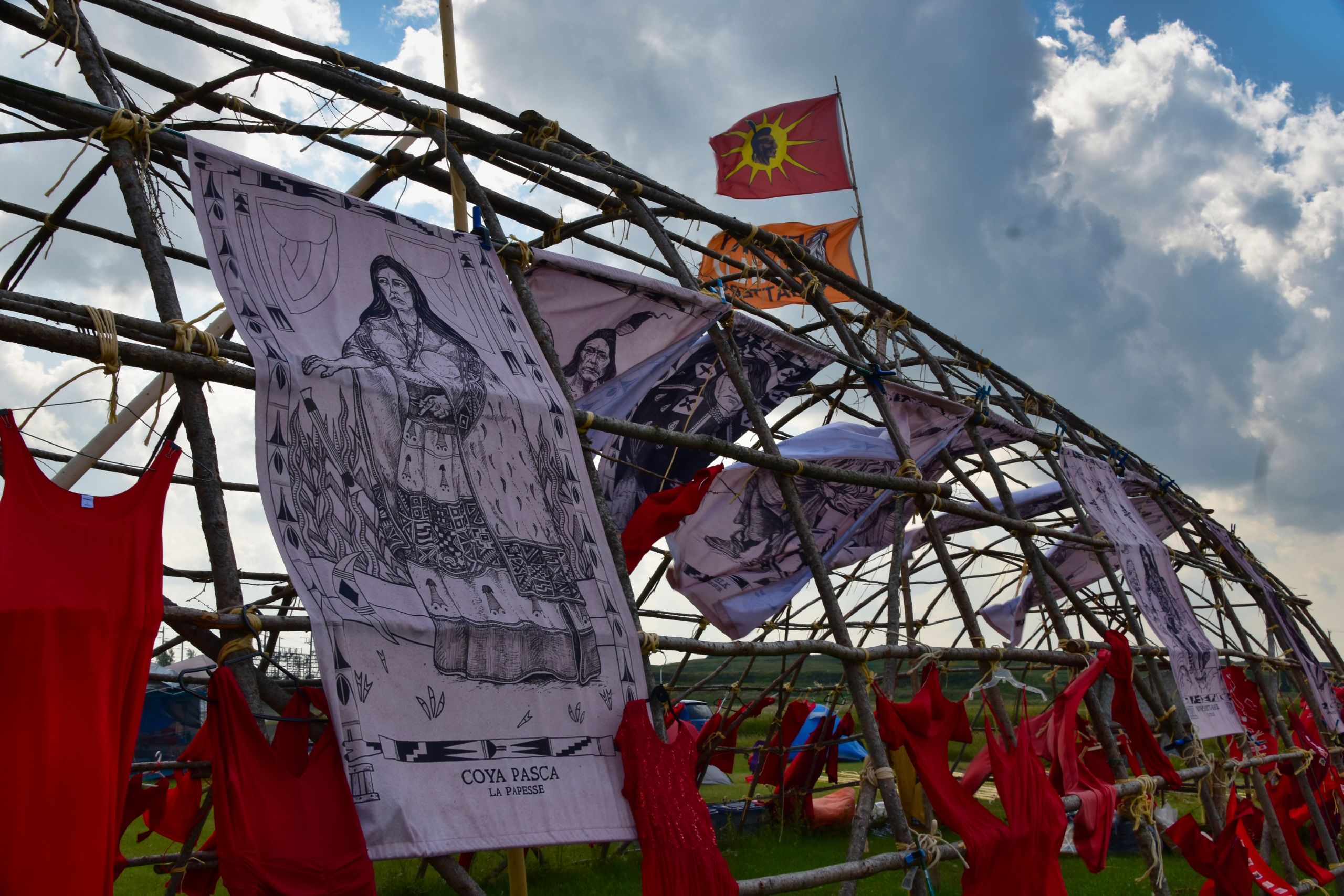 Foto de una estructura longhouse cubierta con vestidos rojos y banderas, en Camp Morgan en el territorio del Tratado 1 ("Winnipeg, Manitoba, Canadá") tomada el 8 de agosto de 2023. Crédito de la foto Jen Deerinwater