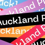 The photo shows a poster for the Auckland Pride Festival. The poster has the word "Auckland Pride" accross several time, and in the colors of the Pride flag. The poster is the official one for the event.