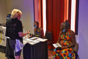 A guest is visiting the Crushing Colonialism table and talking with DeAnna Rhodes