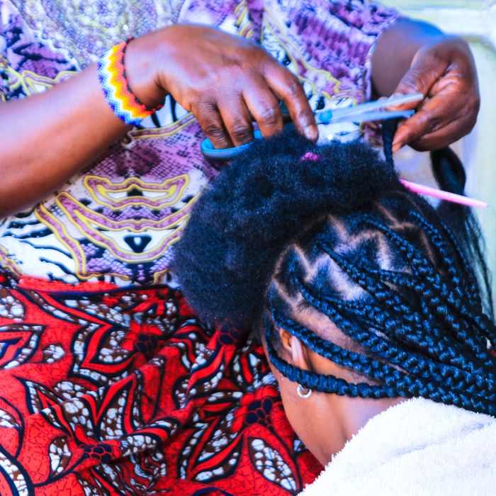 Edna Shaibu sits on the floor and bends her head on the hairdresser’s thighs for her hair to be braided, in a saloon that is located on Buswelu Street, in the Mwanza region, in Tanzania. The hairdresser placed a white towel on Edna’s shoulders to prevent pieces of hair from falling onto her dress. Her half-braided head is exposed to the camera. The photo was taken by George Binagi, on November 4, 2024.