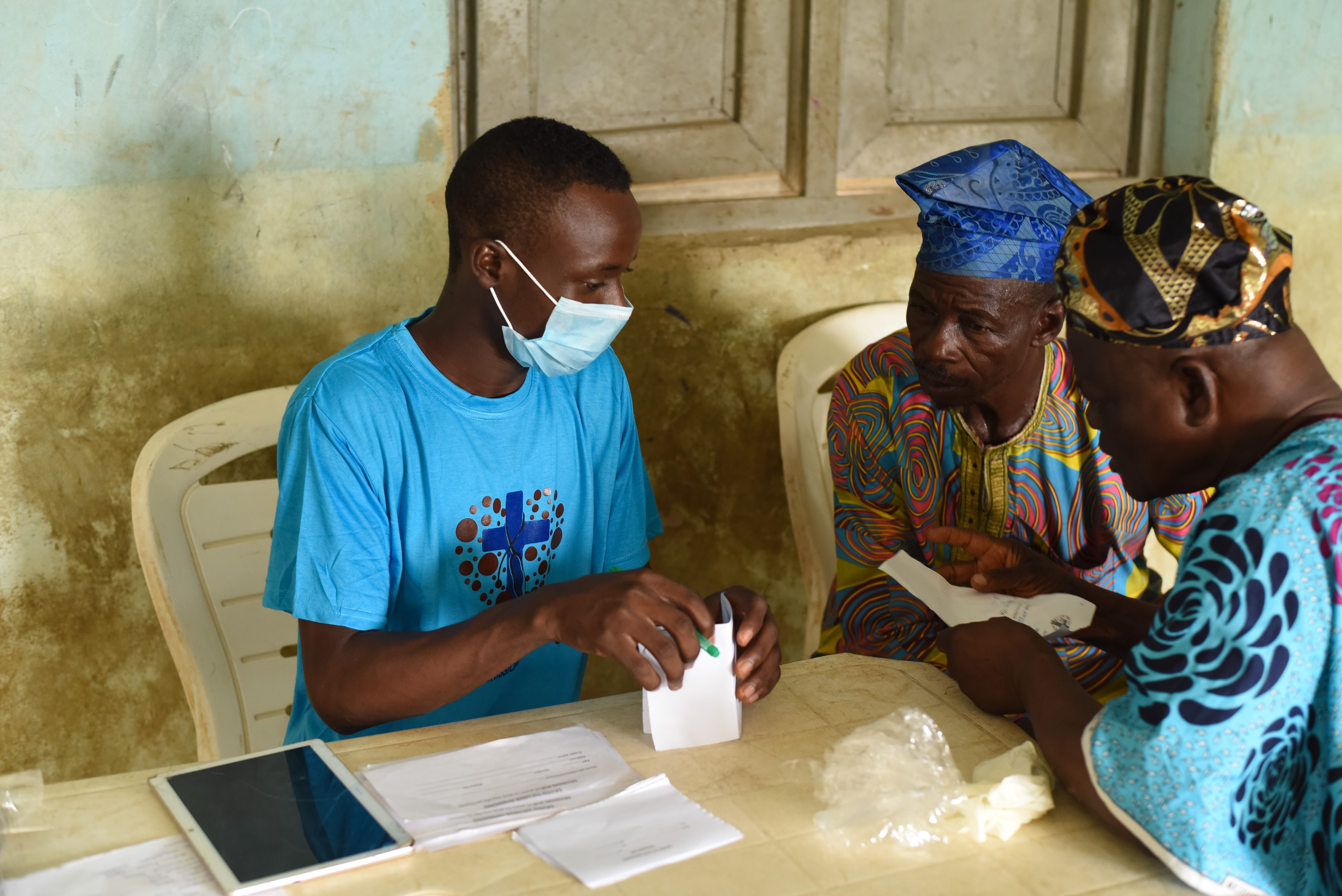 At the registration desk, a medical volunteer digitizes patient information while two community leaders of Langbin review their clinical tracking slips. This initial intake is a critical step in the medical brigade, allowing the team to document patient histories and prioritize those requiring immediate intervention for chronic, water-borne illnesses. Photo credit: Bukunmi Oyewole, December 11, 2020.